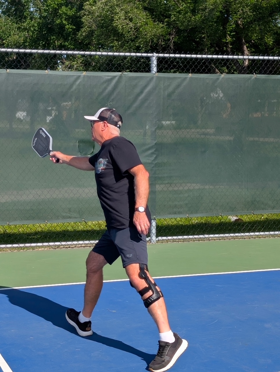 Full-body side view of Tom Rogers playing pickleball with his entire custom knee brace visible
